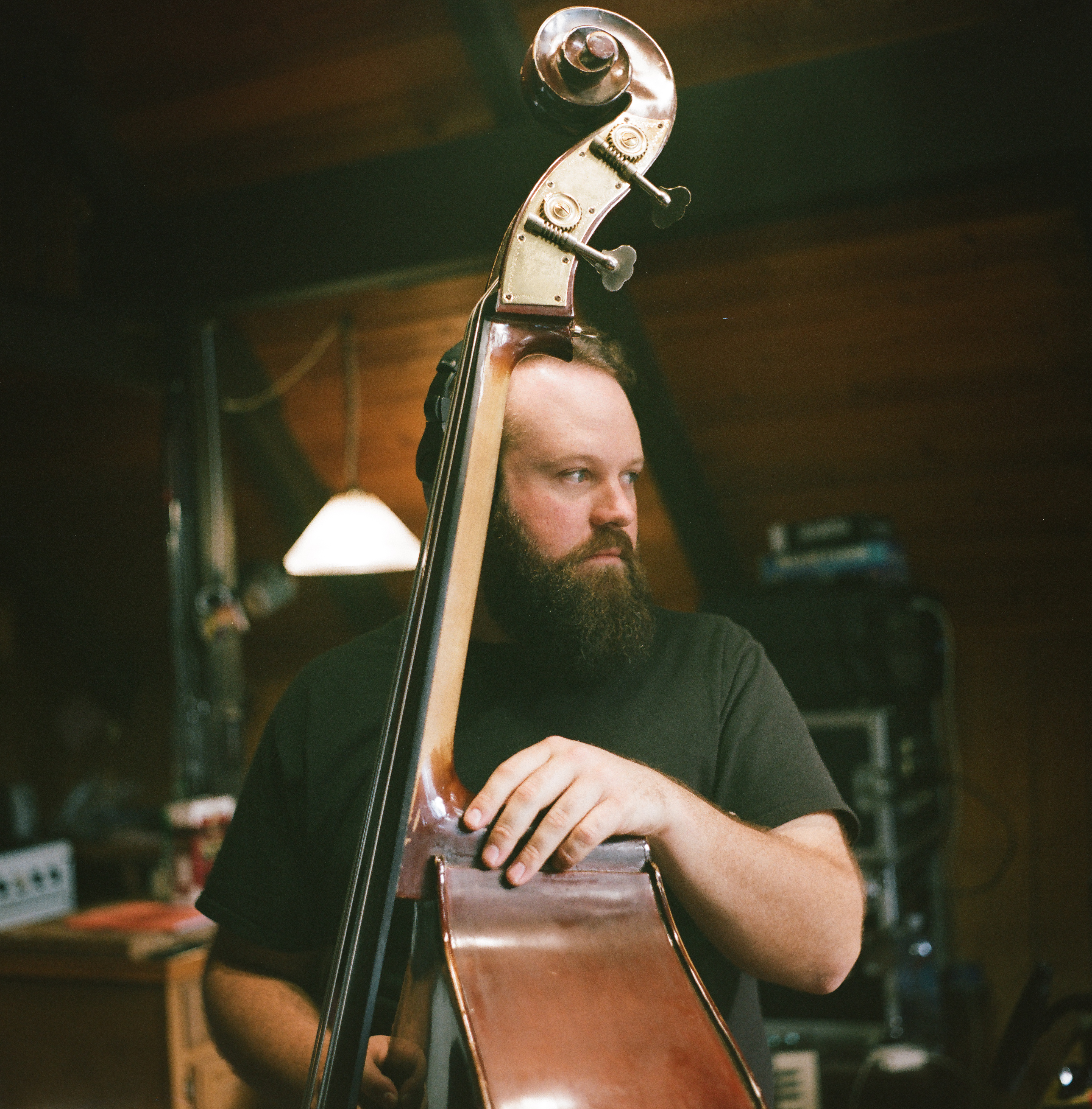 Bass legend Chris Rolontz with his upright bass looking to the right with studio equipment behind him.